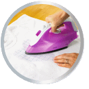 A hand is holding a purple iron, which is being used on a piece of white fabric to smooth out wrinkles.