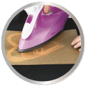 A purple steam iron is pressed onto a brown surface while a hand guides the device.