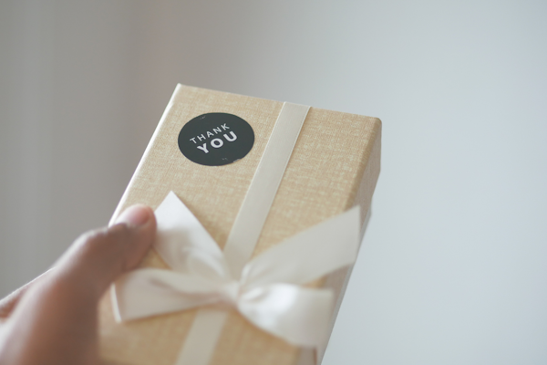 A person is holding a gift with a 'Thank You' sticker and a white ribbon.