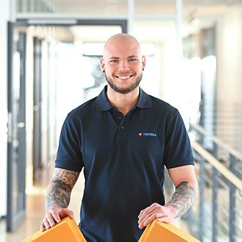 A man with a bald head is wearing a dark blue polo shirt and holding two orange objects in his hands.