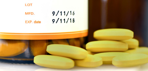 Yellow tablets are next to a small bottle with a label showing the manufacturing date and the expiry date.