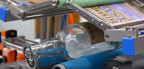 A glass bottle is being processed on a conveyor belt as it gets labelled.