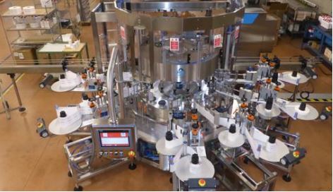 Automatic labelling machine with multiple stations, equipped with a control panel and numerous labelling arms.