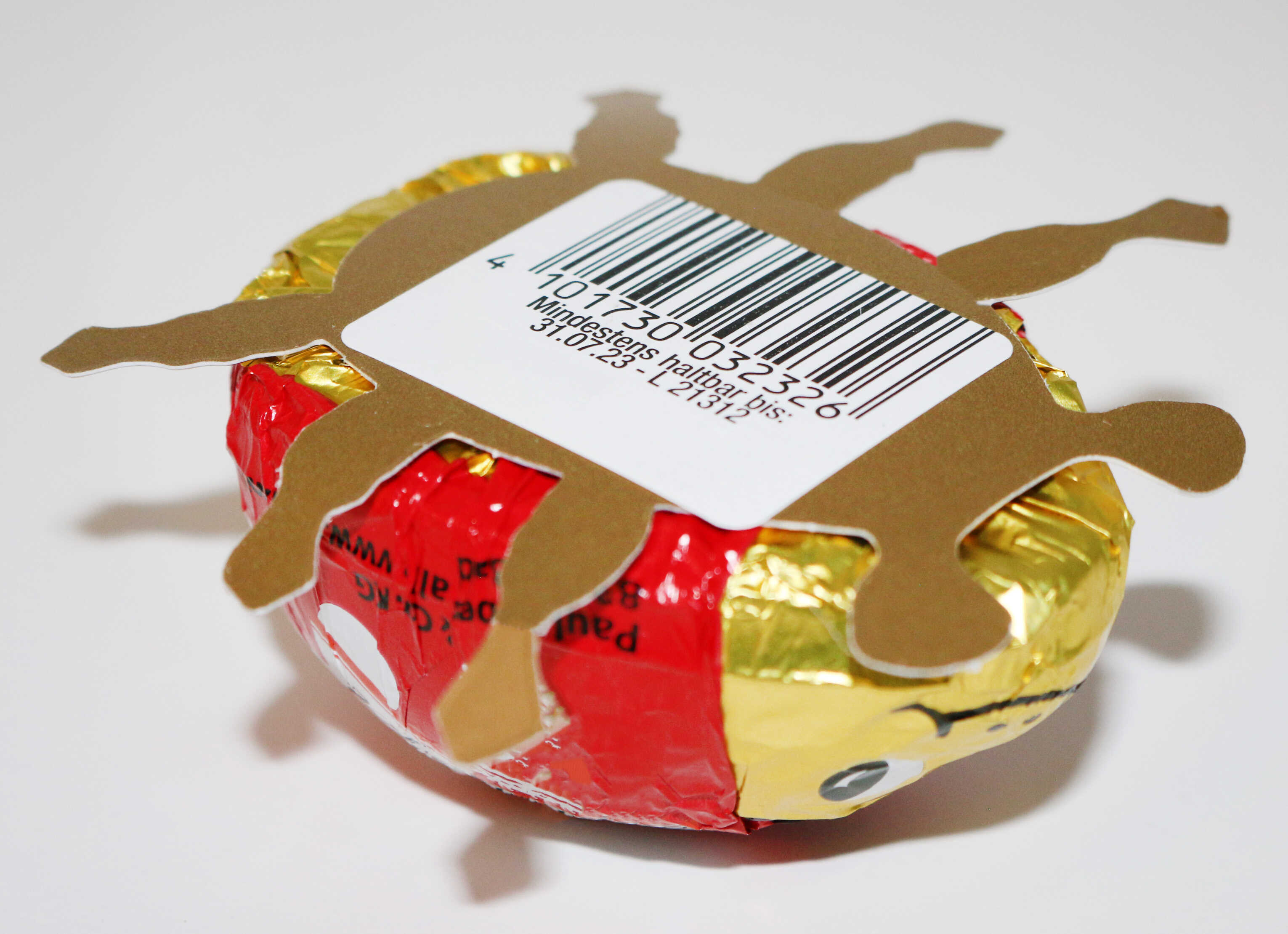 Round chocolate candy wrapped in gold and red foil, decorated with a cardboard figure shaped like a sun and a barcode.