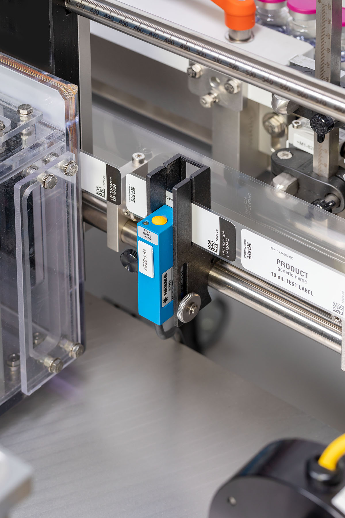 A labelling device with a blue sensor that detects labels on transparent packaging. Several labels are visible.