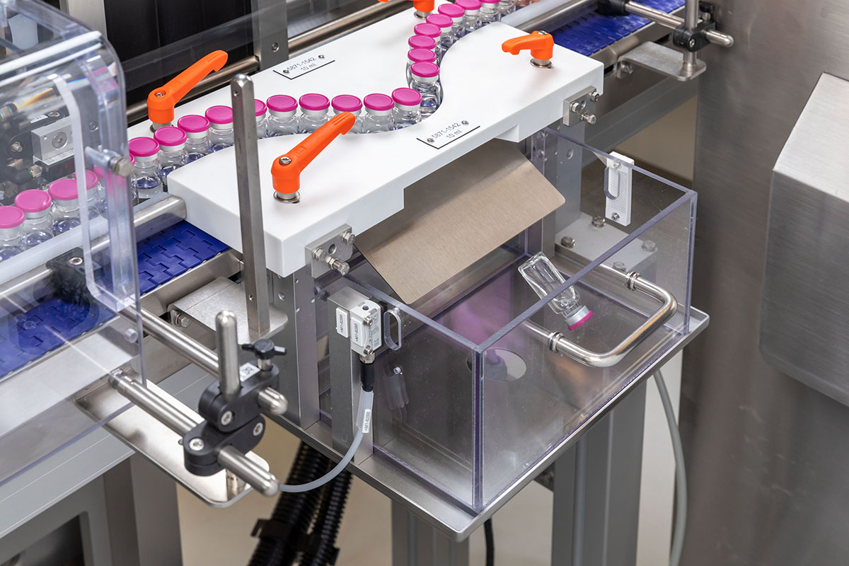 Automated filling system with bottles on a conveyor belt and a container for receiving packaging materials.