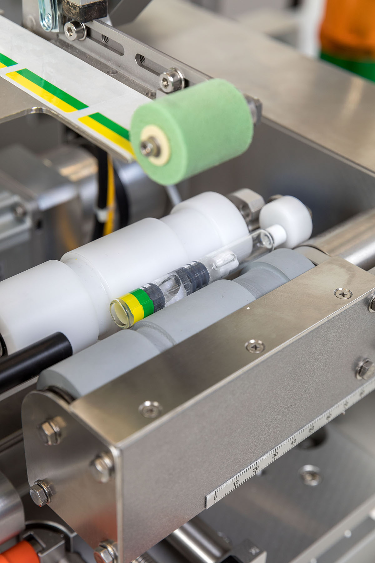 Machine parts with transparent tubes and a green rubber wheel, arranged in an industrial setting.