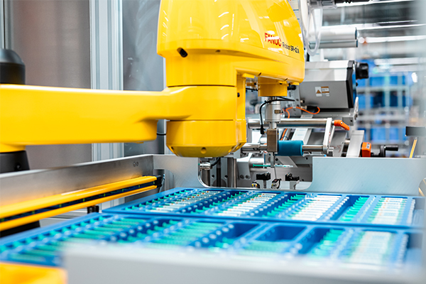 A yellow industrial robotic arm is working on a conveyor belt with blue containers filled with various objects.