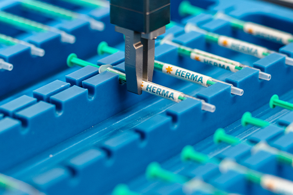 A syringe is labelled and moved with a robotic gripper.
