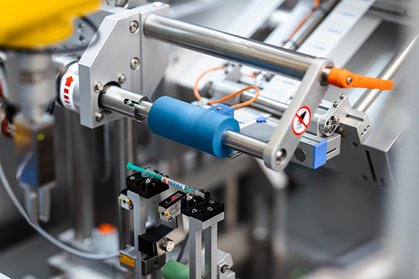 Automated machine components with a blue cylinder and various grippers for handling objects in an industrial environment.