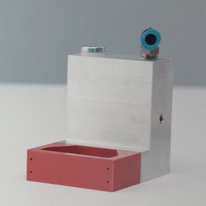 Aluminum component with a red plastic element and connection for compressed air. Ideal for industrial applications.