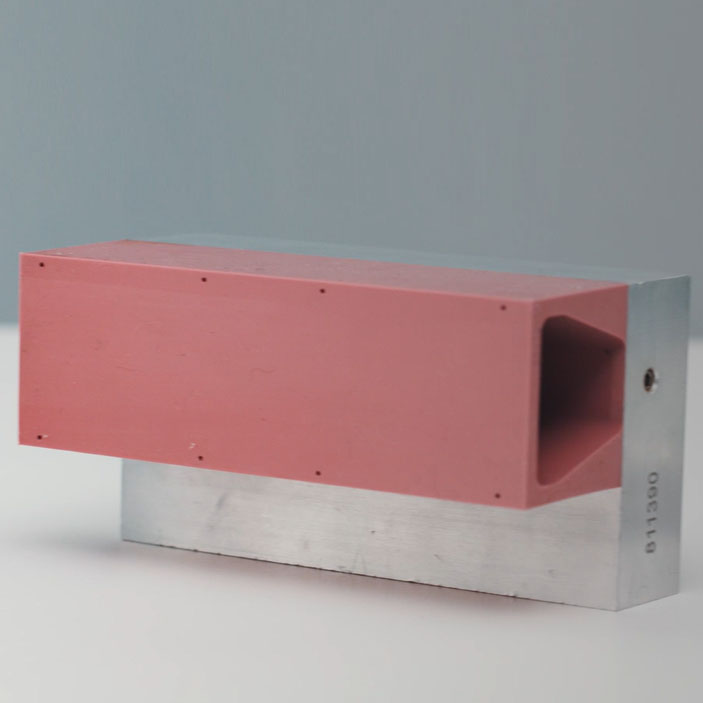 A rectangular block with a red top and a metallic bottom, featuring an opening on one side.