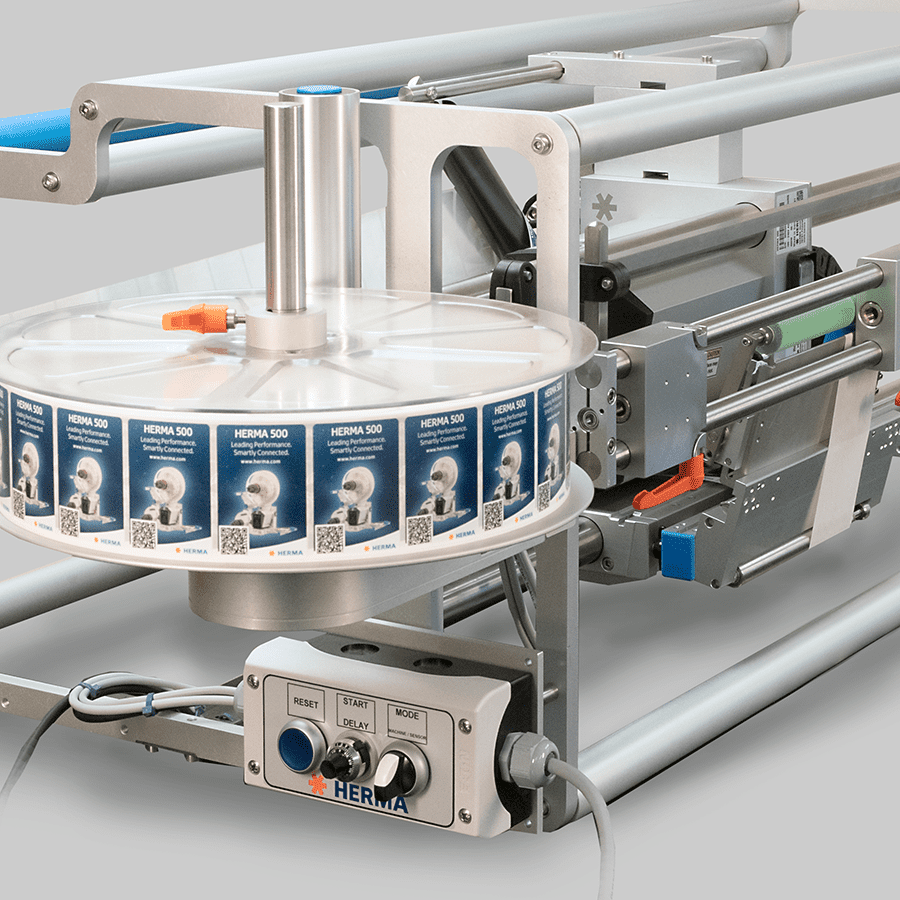 A labelling machine with a roll of labels mounted on a rotating plate and a control panel for operation.