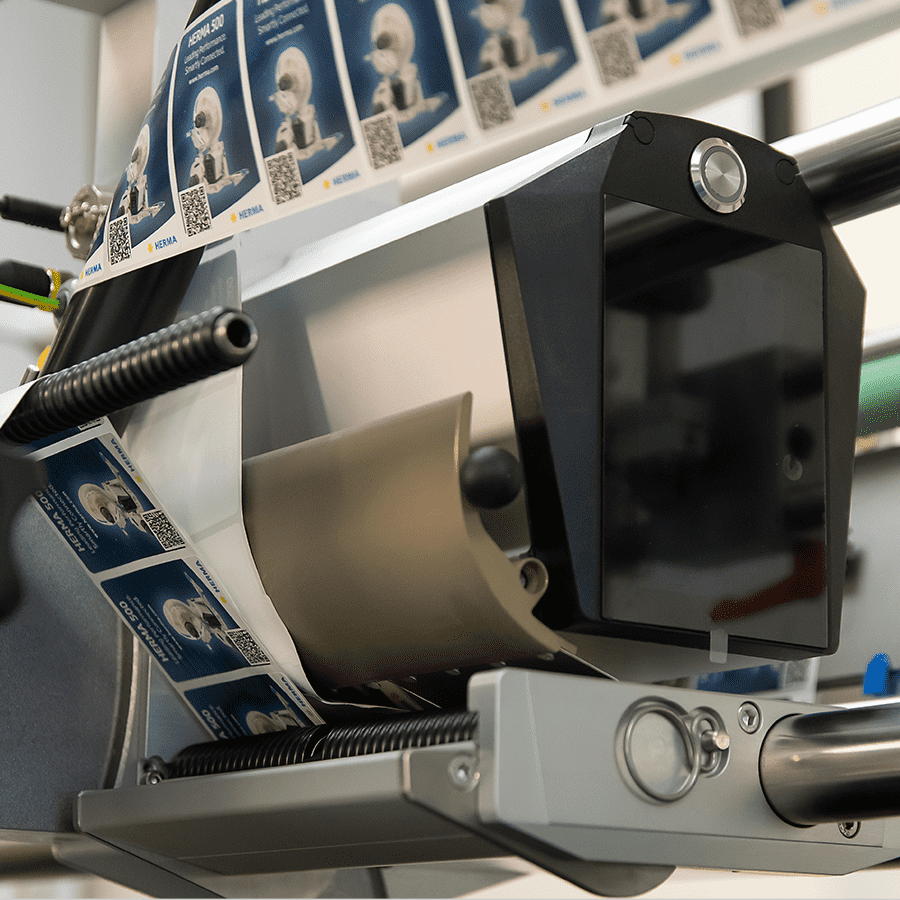 A labelling machine with a roll of labels displaying QR codes and images is ready for use in a production environment.