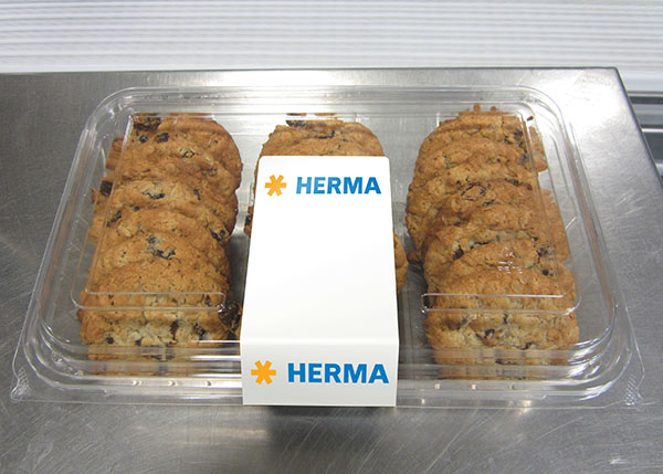 A transparent package containing several chocolate cookies, with a white label in the centre that reads 'HERMA'.