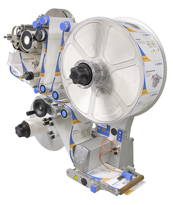 Labelling machine with a large roll of labels, various control elements, and a dispensing mechanism.