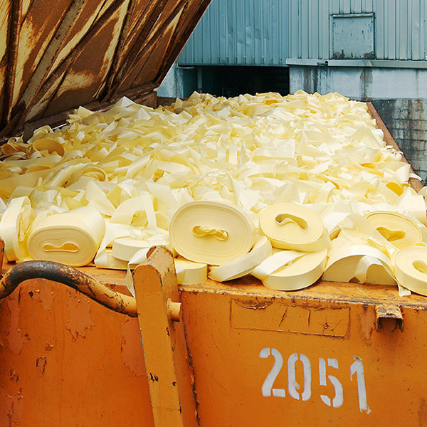 A container filled with yellow plastic strips stacked on top of each other. The container has a rusty surface and a visible number.