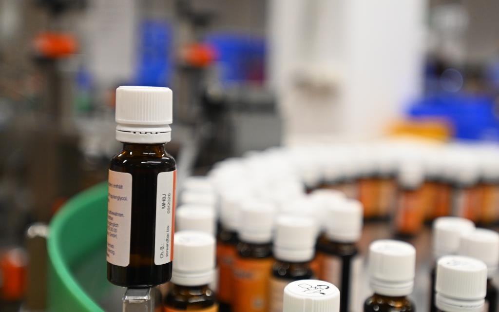 Brown bottles with white caps are lined up in a production line, some bottles are in the foreground while others are in the background.