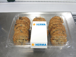 A container filled with several chocolate cookies, with a label in the middle that says 'HERMA'.