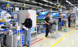 Workers in a production hall, standing at machines and workstations as they carry out various tasks.