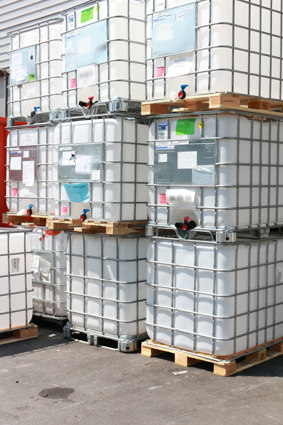 Stacks of large, rectangular plastic containers on pallets, stored in a warehouse area.