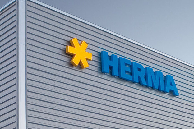 Facade of a modern building featuring the logo 'HERMA' in blue lettering and a yellow symbol.