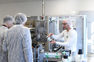 A staff member explains to a group of people in protective gear how to use a container in a production environment.