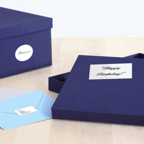 Eine geöffnete, dunkelblaue Geschenkbox mit der Aufschrift „Happy Birthday!“ und zwei Umschlägen in hellblau und grau daneben.