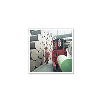 A woman operates a forklift in a warehouse to move large rolls of paper, while more rolls are stacked in the background.