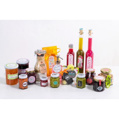 Eine Auswahl an verschiedenen Gläsern mit Marmelade, Saucen und Gewürzen, ergänzt durch Flaschen mit Öl und einem Geschenkbeutel.