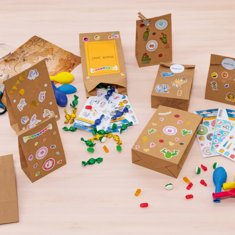 Colorful gift bags and craft supplies on a table, including stickers, balloons, scissors, and candies.