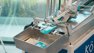 Automated machine for packaging products, featuring an open container for receiving packaged items.