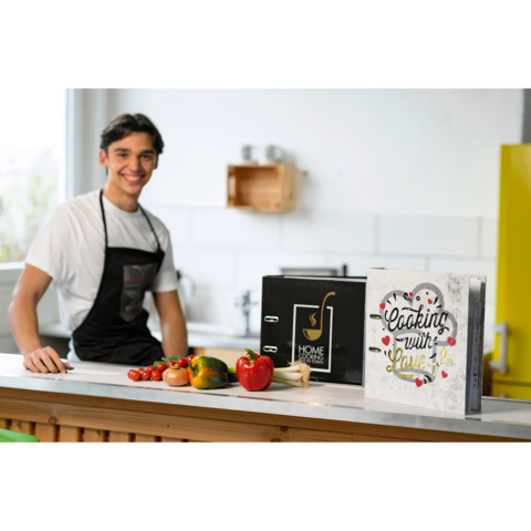 Ein junger Mann in einer Schürze steht an einer Küchentheke mit frischem Gemüse und einem Kochbuch mit dem Titel "Cooking with Love".