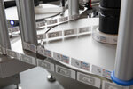 A labelling machine with multiple rollers that applies labels to a conveyor belt surface. The labels display various information.