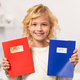 A smiling child holds a red notebook and a blue notebook in their hands, both covered in stickers.