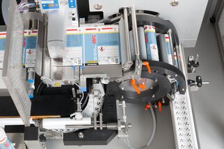 An industrial labelling machine with various rollers and a conveyor belt, used for labelling products.