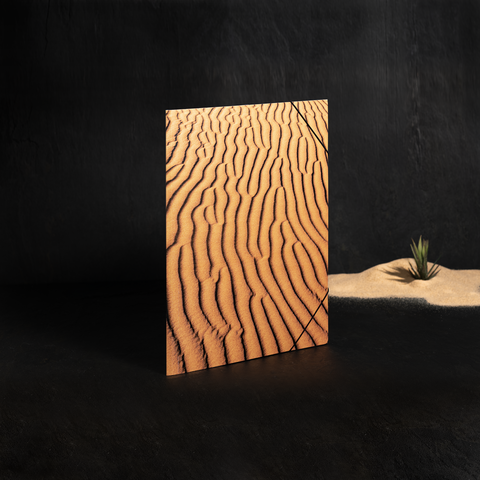 Ein Notizbuch mit einem Cover, das Wellenmuster im Sand zeigt, steht auf einem dunklen Hintergrund.