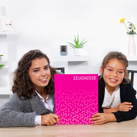Two girls are sitting at a table, holding a pink notebook with the title 'TESTIMONIALS' on it. They are smiling at the camera.