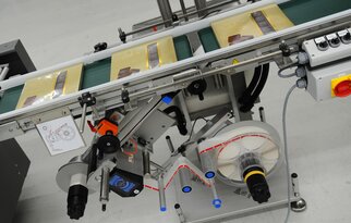 A conveyor belt with packaged products, equipped with a labelling machine and various control elements.