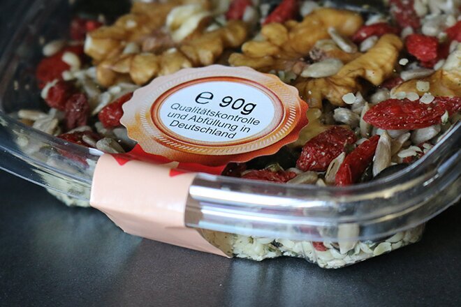 A transparent bowl filled with a mix of nuts, seeds, and dried fruits, labelled with nutritional information.
