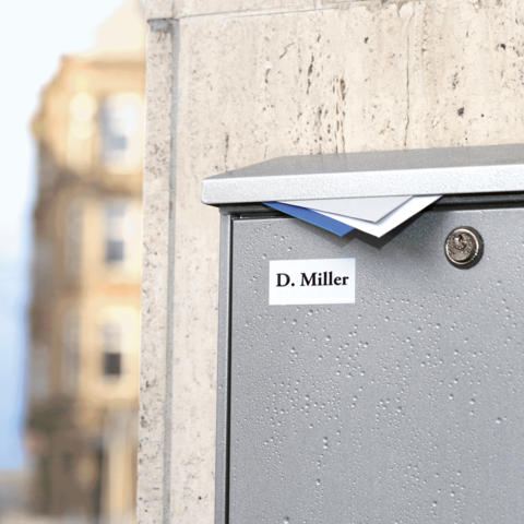 Briefkasten mit dem Namen "D. Miller" auf einer Wand, leicht feucht, mit Briefen, die teilweise herausragen.