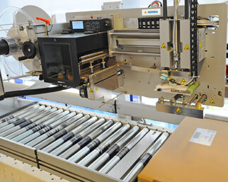 A labelling machine with a roller conveyor that applies labels to packages. The machine features digital controls and safety warnings.