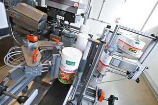 Machine for filling organic butter into containers, featuring various mechanical components and labelling stations.