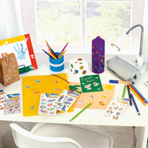 Colorfully decorated desk with craft supplies, stickers, pens, a binder, and a lamp.