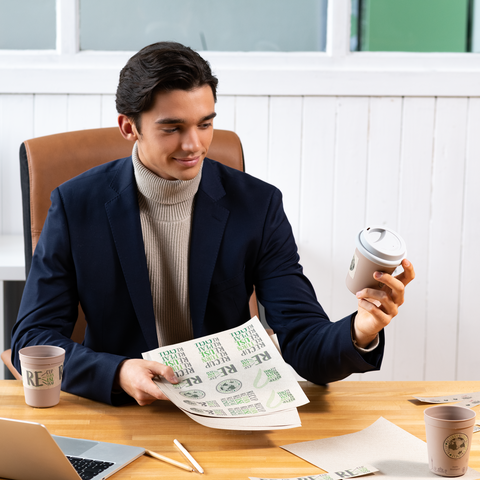 A young man in a suit is holding a coffee cup and a piece of paper with text in an office setting.