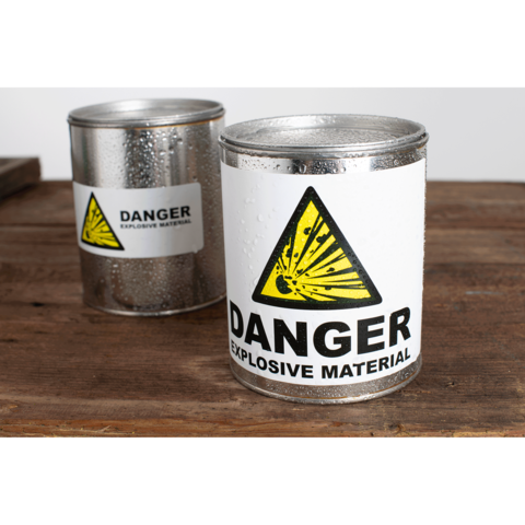 Metallbehälter mit Warnaufkleber "DANGER EXPLOSIVE MATERIAL" auf einem Holztisch, einer mit Kondenswasser.