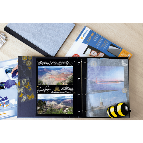 Ein offenes Fotoalbum mit Bildern von Landschaften, einer Geburtstagsnachricht und einem Bienenmotiv. Daneben liegt ein Fotopapierpaket.