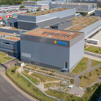 Modern industrial buildings with green roofs and the Merima logo, surrounded by streets and green spaces.