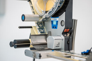 Labelling machine with rollers, control elements, and a display, ready for labelling products.