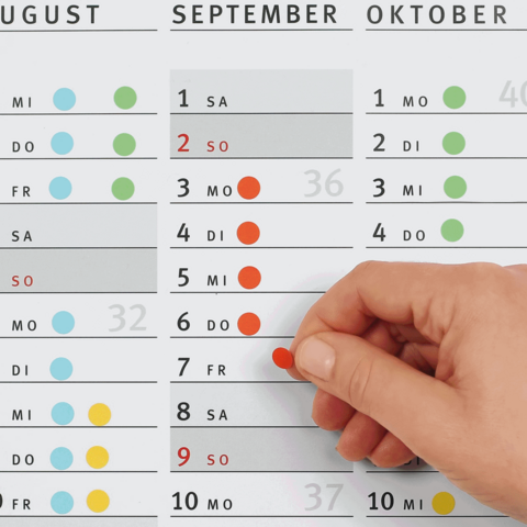 Kalender mit Monaten August, September und Oktober, hand zeigt auf den 7. September. Zahlen und farbige Punkte markieren bestimmte Tage.